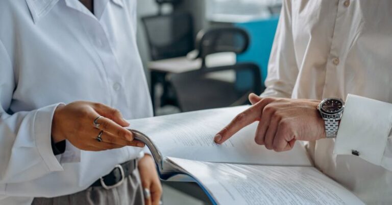 Accounts Management - Colleagues Standing in White Long Sleeve Shirts Discussing and Reading a Financial Report