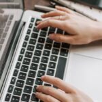 Technical SEO - From above of unrecognizable woman sitting at table and typing on keyboard of computer during remote work in modern workspace