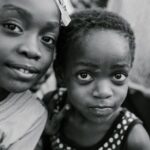 Authentic Content - Black and white glad children in casual clothes standing on authentic town street and looking at camera with curiosity