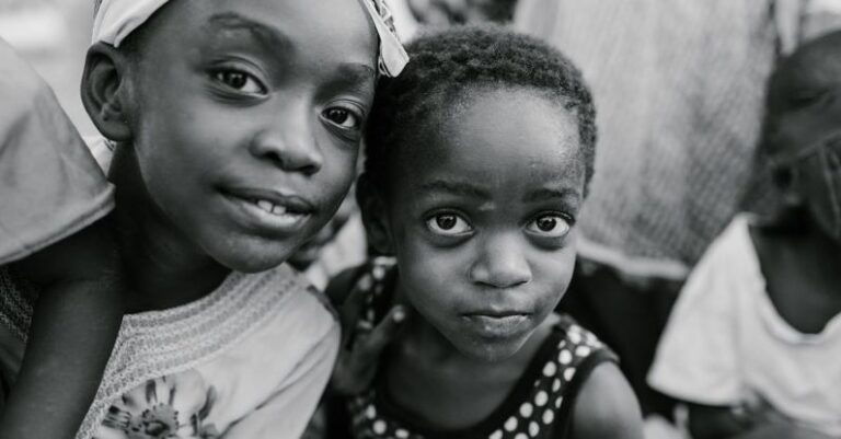 Authentic Content - Black and white glad children in casual clothes standing on authentic town street and looking at camera with curiosity