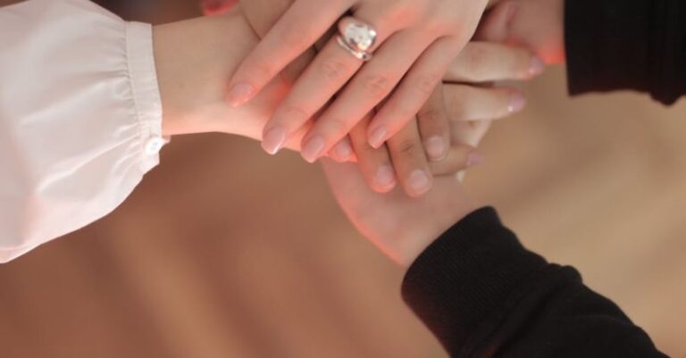 Brand Trust - Top view of faceless friends in different clothes stacking hands together while standing on wooden floor indoor on sunny day