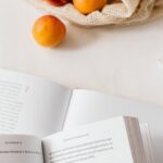 Product Pages - Jute sack with appetizing ripe apricots placed on table with different books